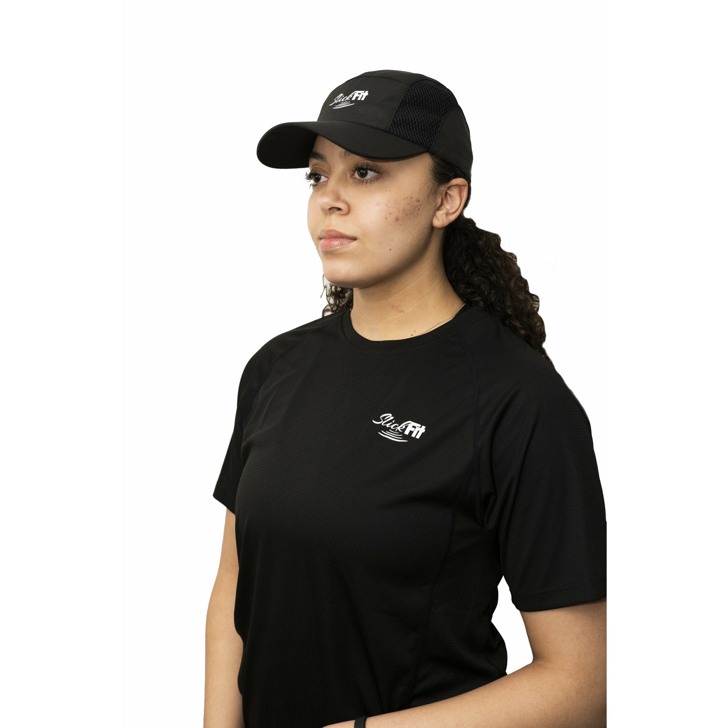 Woman with curly hair in black SlickFit satin lined baseball cap and activewear shirt looking into distance
